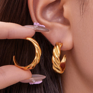 Gold twisted hoop earring worn on ear with matching earring held by hand, close-up jewelry detail