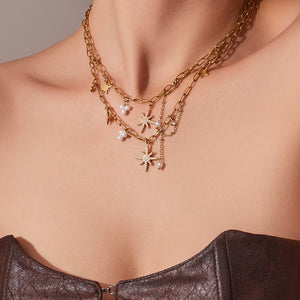 Close-up of layered gold necklaces with star and pearl charms on a woman's neck wearing a brown textured strapless top