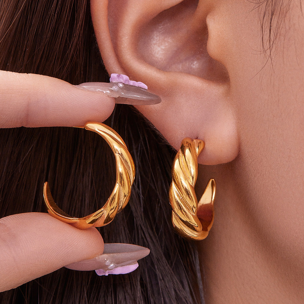 Gold twisted hoop earring worn on ear with matching earring held by hand, close-up jewelry detail