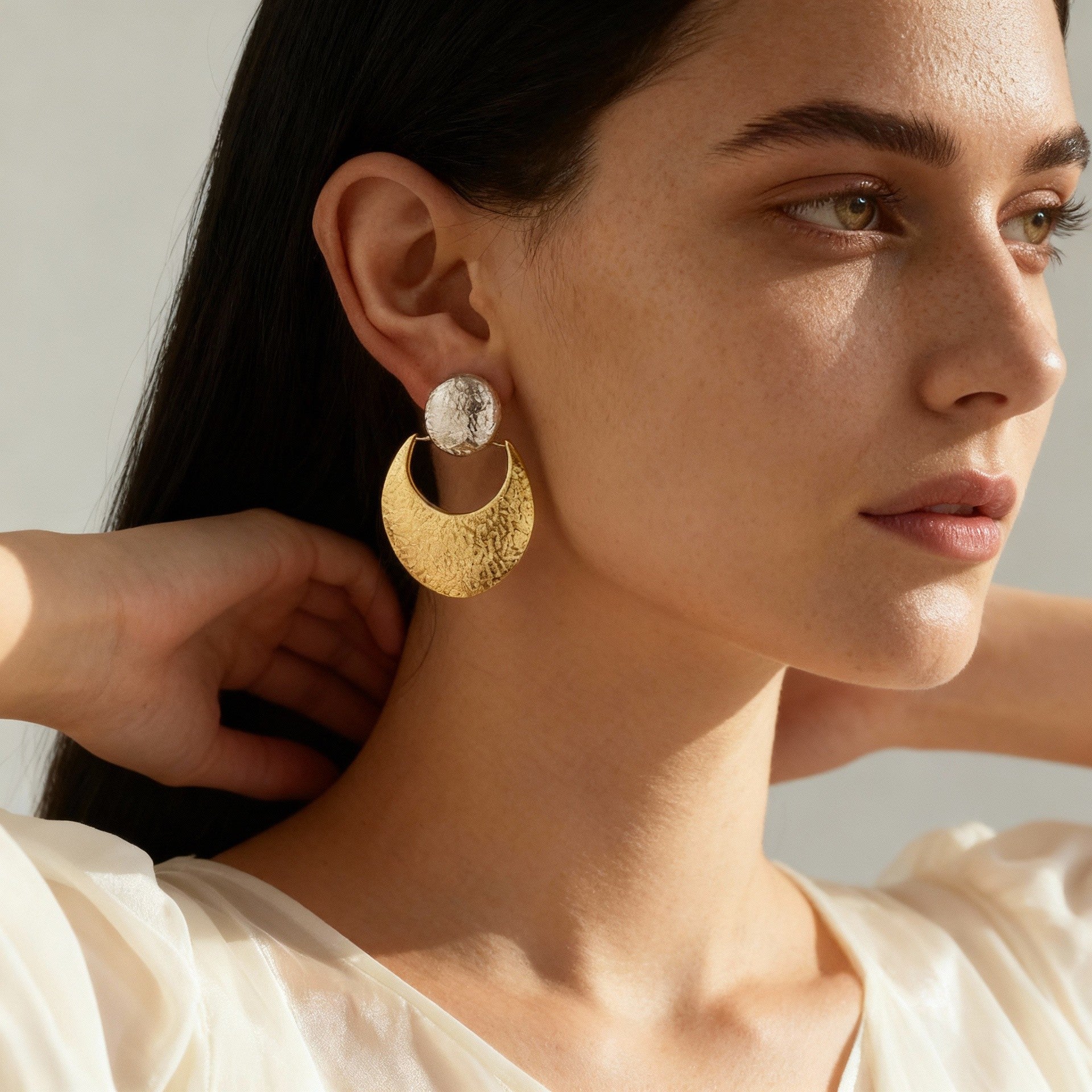 Close-up of a woman wearing textured silver and gold crescent moon earrings, showcasing TycheLuck's spiritual jewelry collection